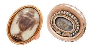 At left is a 19th-century memorial ring mounted in 14-karat gold. Its design features an urn composed of hair that is accented by seed pearls within  a glazed compartment. To the right is a 10-karat gold snake motif memorial brooch centring a coiled lock of hair within a glazed frame and surrounded by a split-pearl ouroboros.