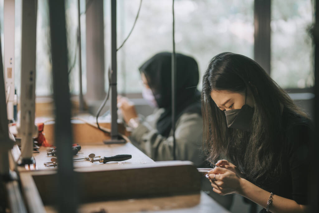 Two female college student side by side crafting jewelry at a workbench